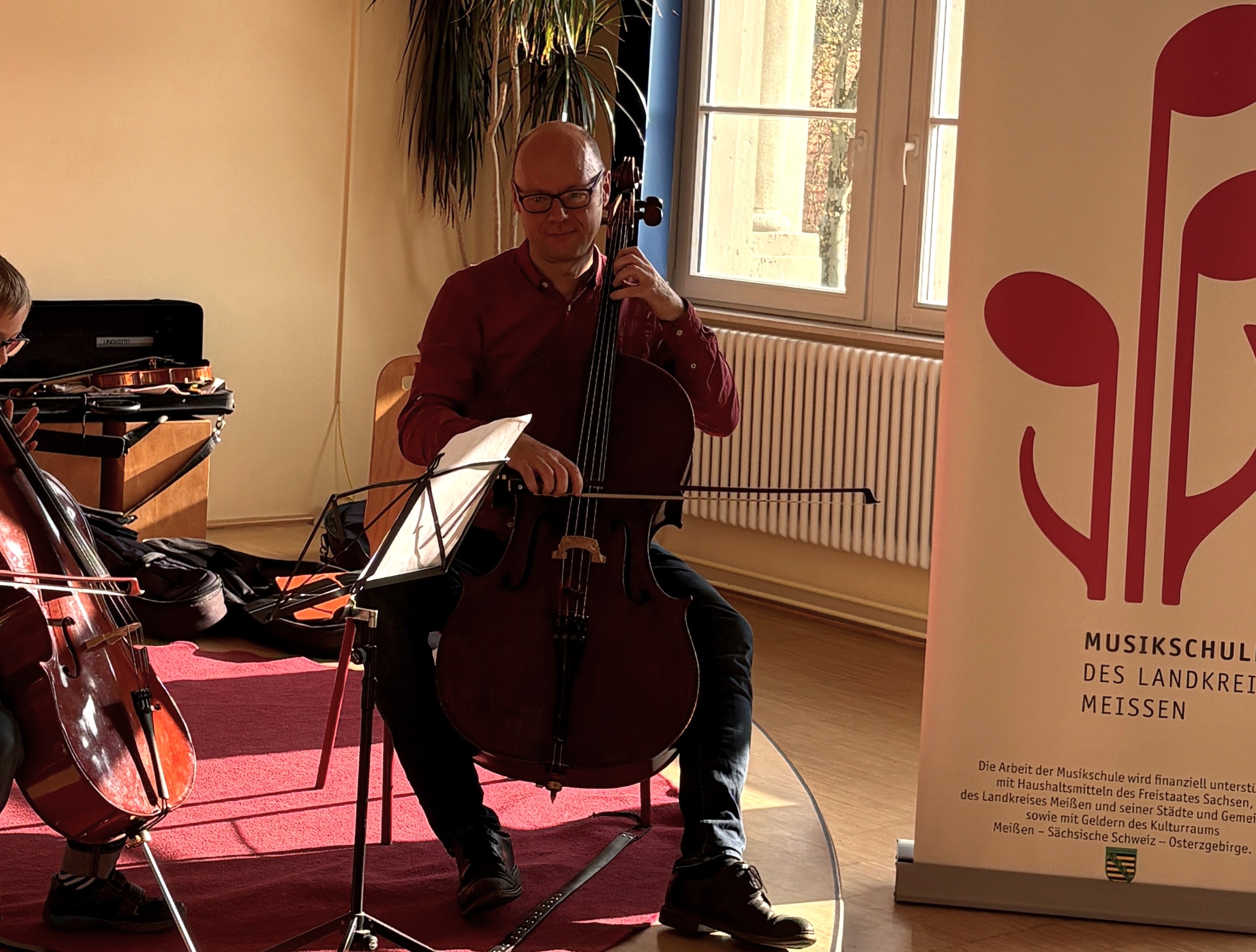 Ein Lehrer musiziert zusammen mit seinem Schüler. Beide spielen Cello.